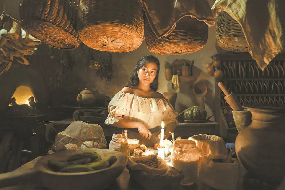 A woman cooking in a kitchen scene from the TV series One Hundred Years of Solitude, showcasing cultural culinary traditions.