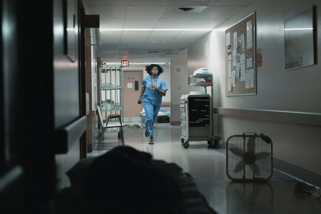 Woman running down a hospital corridor in "Five Days at Memorial," conveying urgency and tension in a medical crisis.