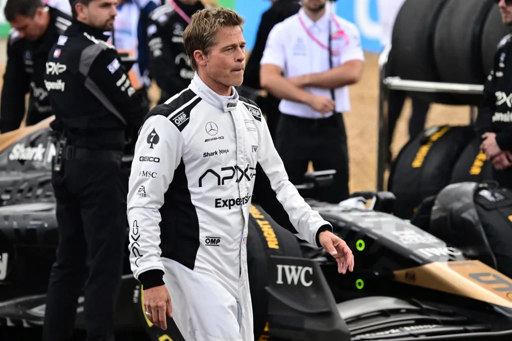 Brad Pitt dressed in a race fit, posing beside a stylish F1 car, showcasing a cool and dynamic racing vibe.